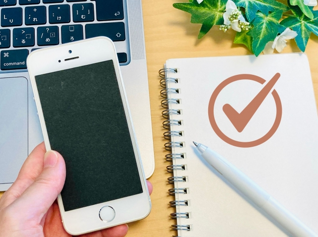 An iPhone being held next to a notebook with a big red check mark on it.