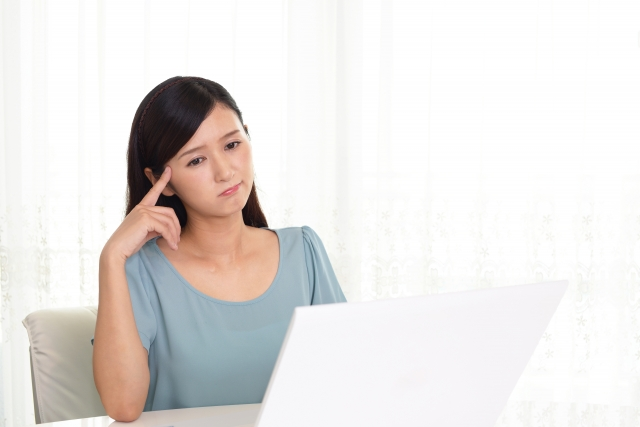 Woman looking at a white laptop with an upset look on her face, and her hand on her hand like she is upset.