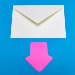 An envelope sits on a blue background with a pink arrow made of paper placed beneath it pointing downwards.