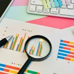 A desk scattered with colourful graphs and a magnifying glass on top.