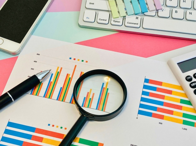 A desk scattered with colourful graphs and a magnifying glass on top.