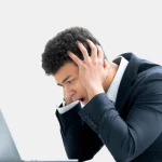 A man in a business suit appears stressed while looking at a laptop.