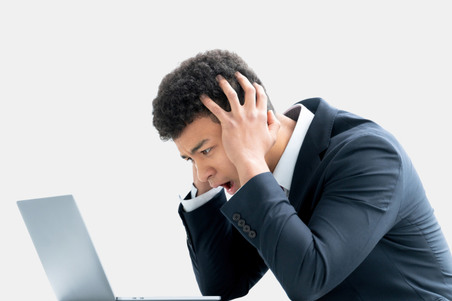 A man in a business suit appears stressed while looking at a laptop.