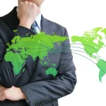 A salary man standing with his fist under his chin with a world map superimposed over him.