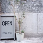 A wooden board with "OPEN" and open hours painted on it in black.